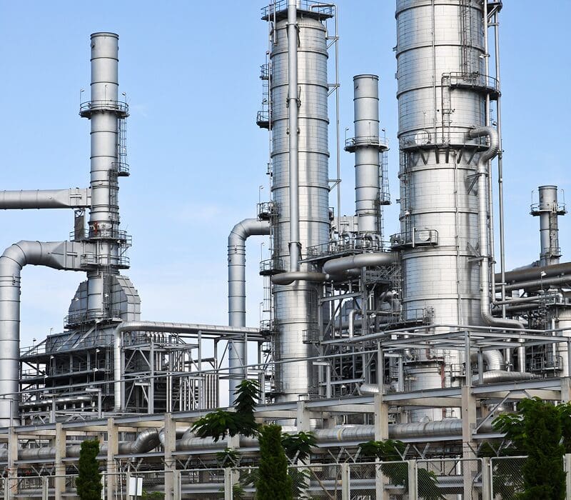 Oil refinery with large tanks and pipes in the middle of it, surrounded by trees