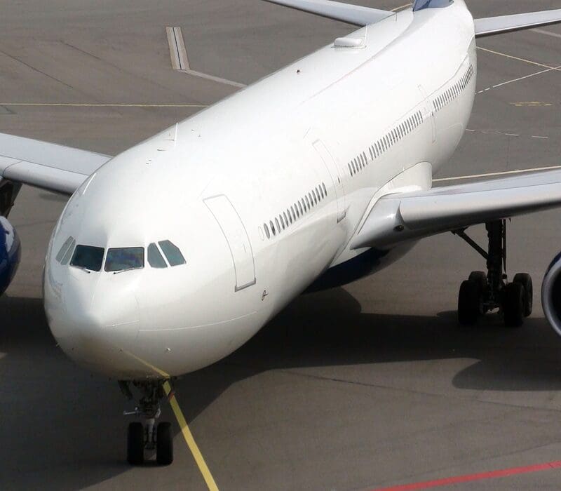 Large white airplane sitting on top of an airport tarmac, with another airplane visible on the left side