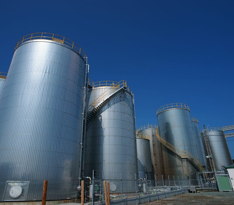 Large group of large metal silos sitting next to each other, with a fence in the foreground